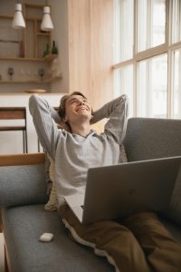Smiling man reclining on a sofa with a laptop, enjoying a relaxed day at home.